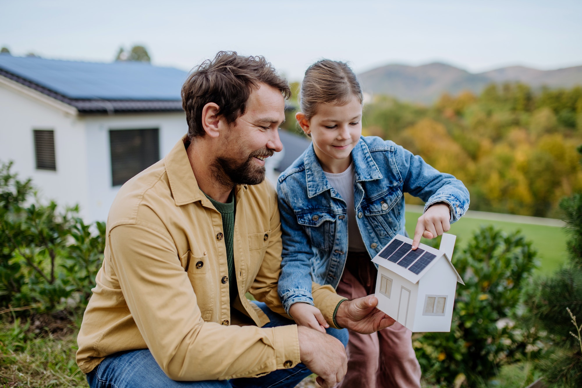 Niña con su papá sosteniendo un modelo de papel de una casa con paneles solares, explicando cómo funciona
